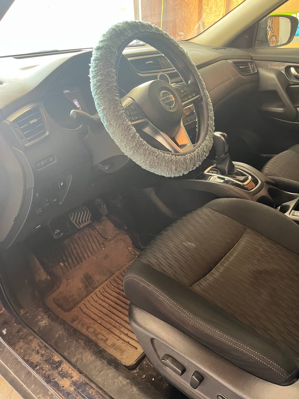 Driver's side footwell of a blue Nissan Rogue before cleaning, the ribbed rubber mat caked in dried mud and the door sill covered in dirt