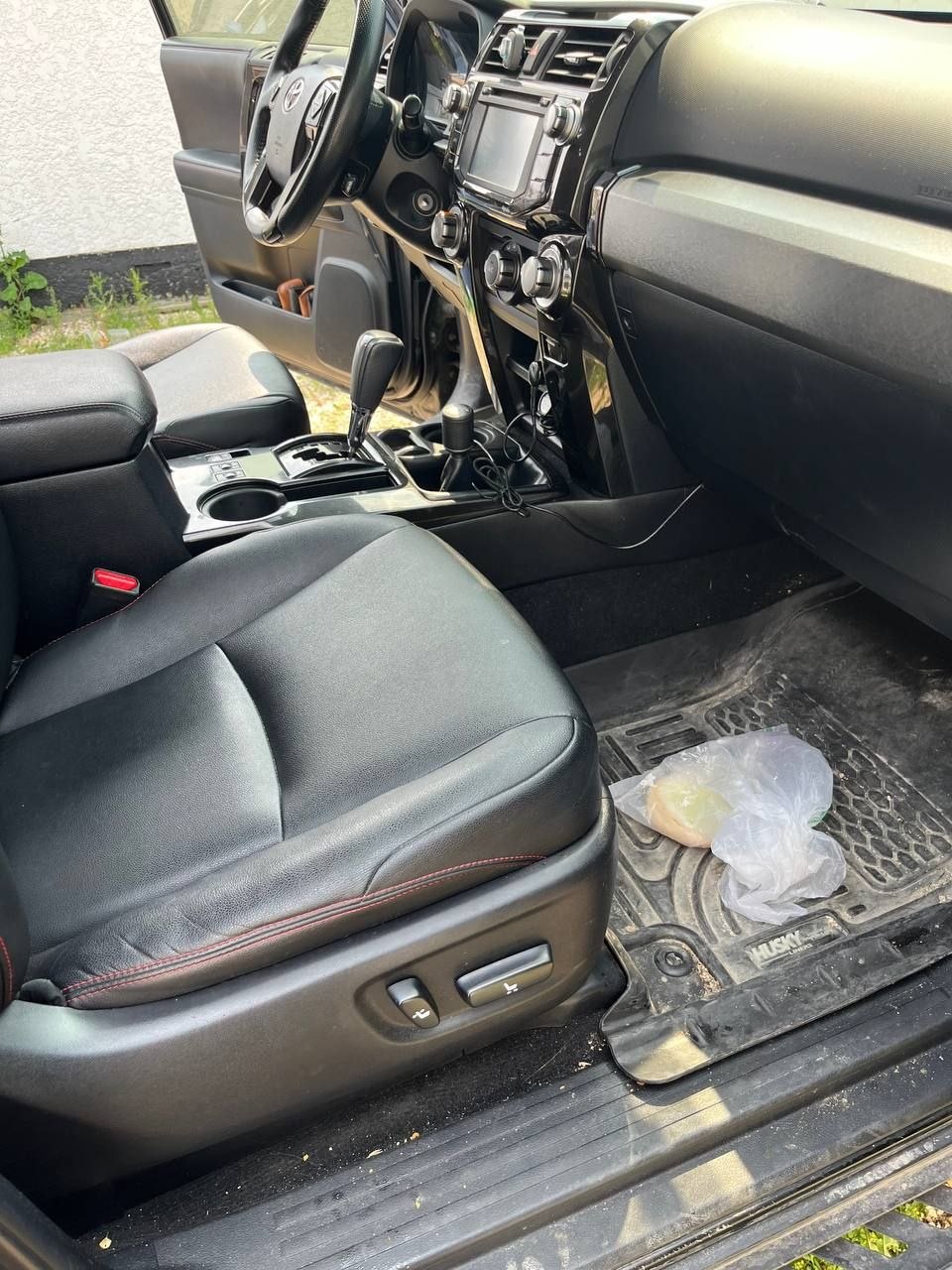 Passenger side of a black Toyota 4Runner before cleaning, with a plastic bag and litter sitting on the rubber floor liner and grit along the door sill