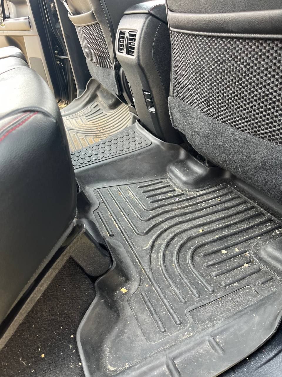 Rear footwell of a black Toyota 4Runner before cleaning, crumbs and grit scattered across the moulded rubber liner