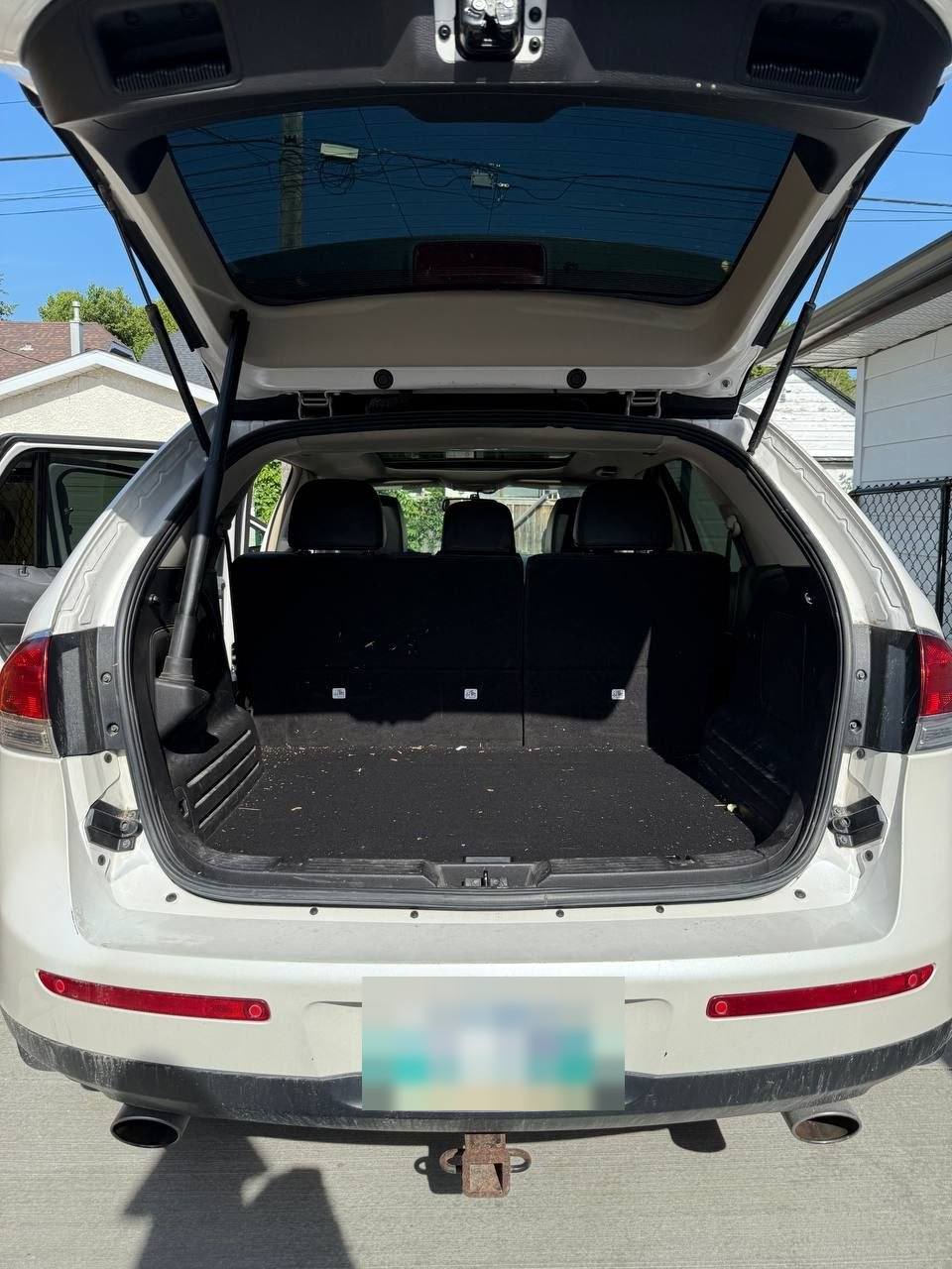 Cargo area of a white Lincoln MKX before cleaning, with dried leaves and grit worked into the carpet